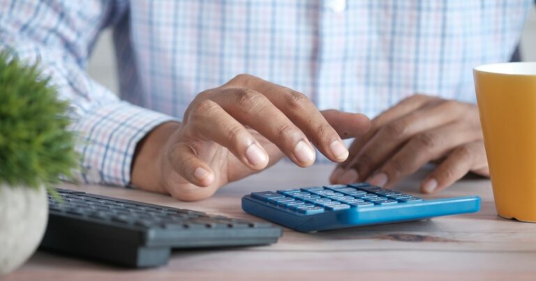 person using calculator at desk with coffee mug