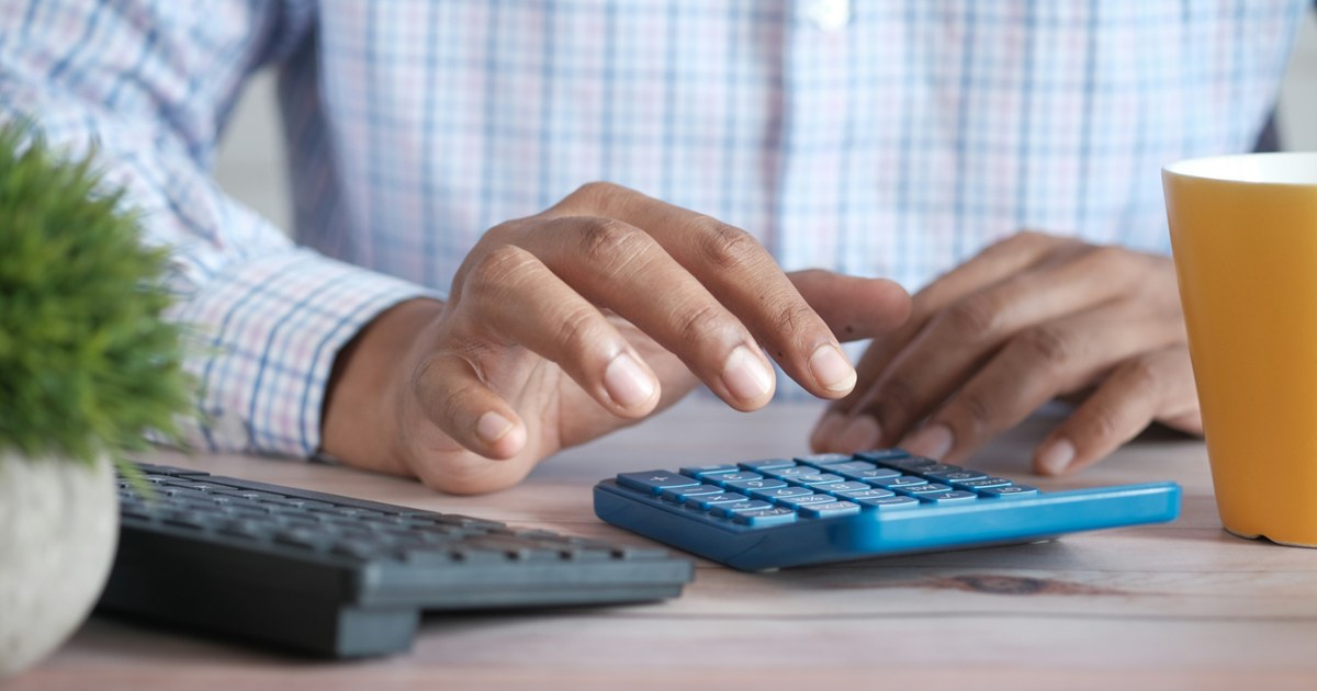 person using calculator at desk with coffee mug