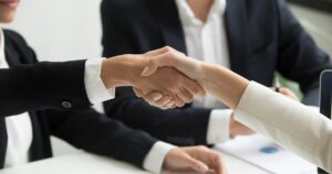 two people shaking hands in front of a laptop