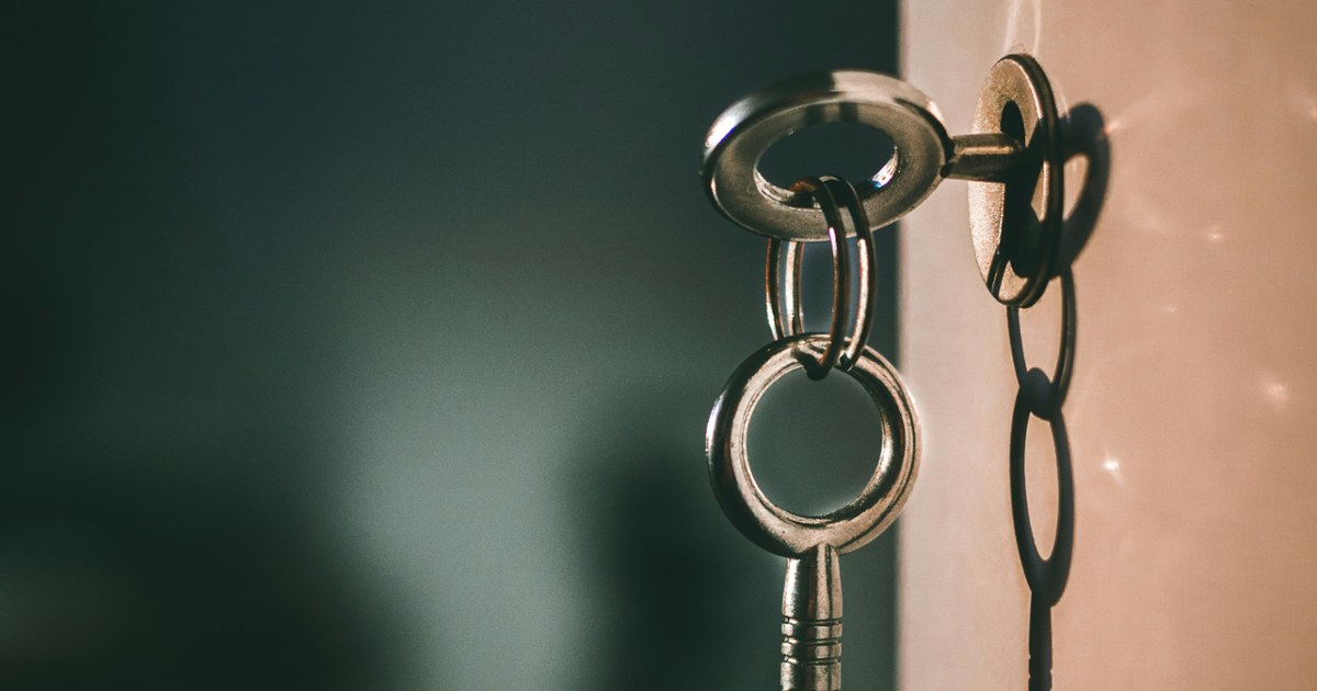 A metal key in a keyhole with a shadow on a wall